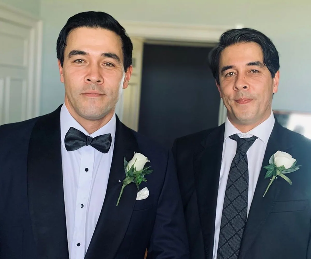 Two formally dressed men with matching rose boutonnieres smiling at the camera.