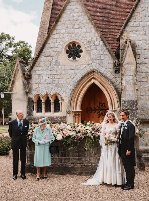 "Princess Beatrice and husband in wedding attire outside a stone chapel with two elder guests nearby."