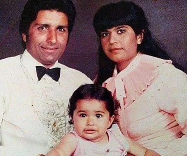 A man in a tuxedo and a woman in pink posing with a baby wearing a pink dress, all facing the camera.