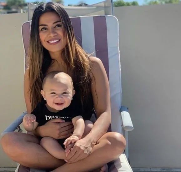 Woman sitting outdoors on a lounge chair, holding a smiling baby on her lap.