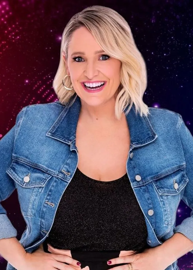 A woman with short blonde hair smiles, wearing a denim jacket and black top against a vibrant, colorful background.