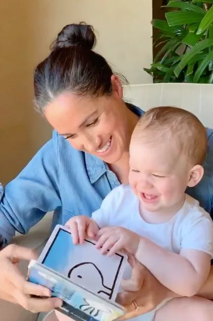 Woman in denim shirt reads a children's book with a smiling baby on her lap.