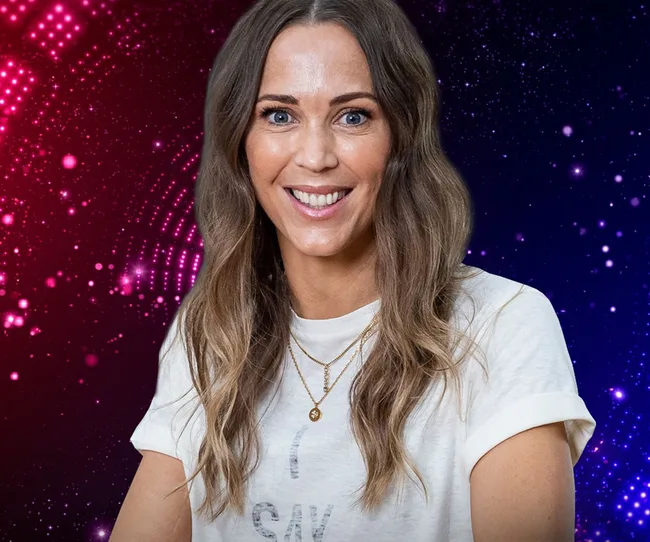 Woman smiling against a neon red and blue dotted background, wearing a white shirt and layered necklaces.