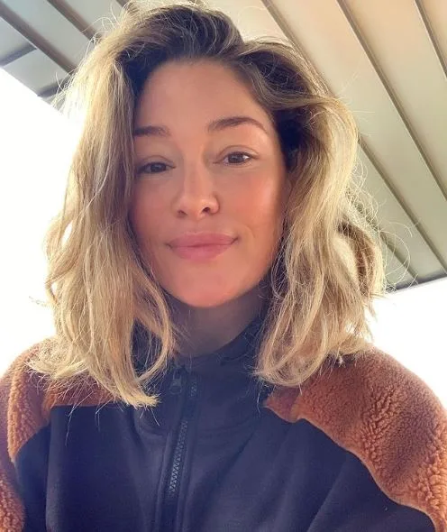 I don't know who this person is, but they're taking a casual selfie with natural lighting and a brown and black jacket.