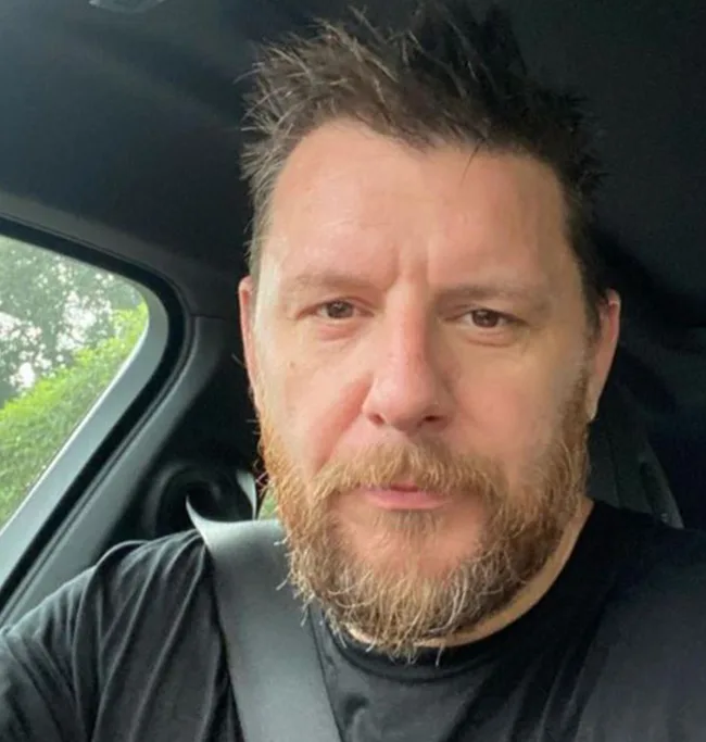 Person with a beard in a car, wearing a seatbelt, in a casual setting.