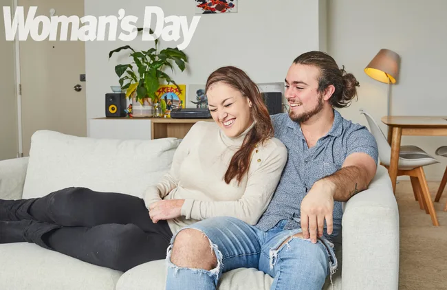 Couple sitting on a couch, smiling and relaxed, in a cozy living room setting.