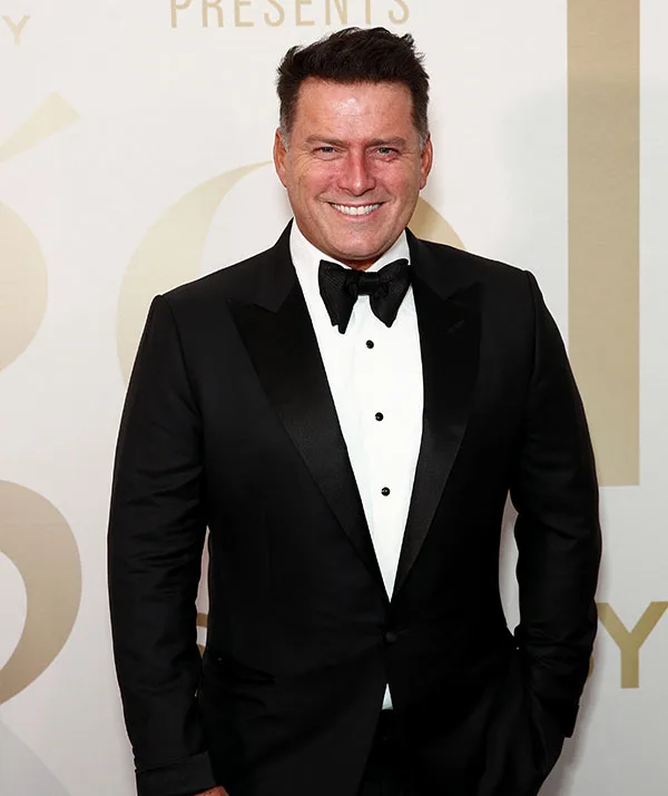 Man in a black tuxedo with a bow tie, smiling at an event.