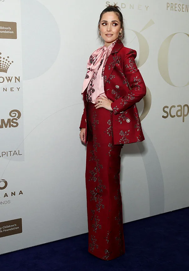 A person in a red floral suit with a pink blouse poses at an event.