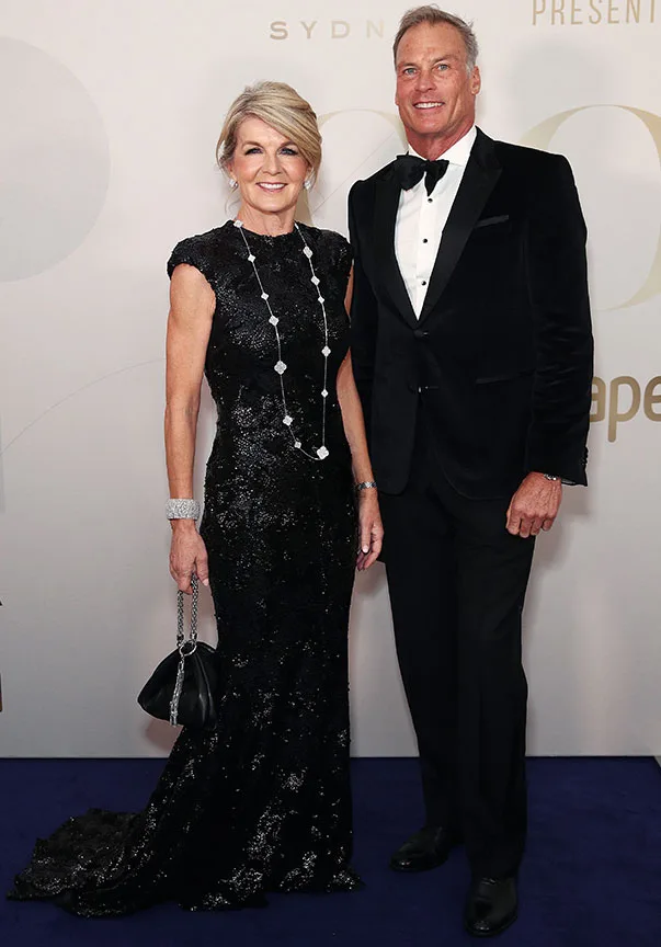 A woman in a black sequin dress and a man in a black tuxedo pose on the red carpet at an event.