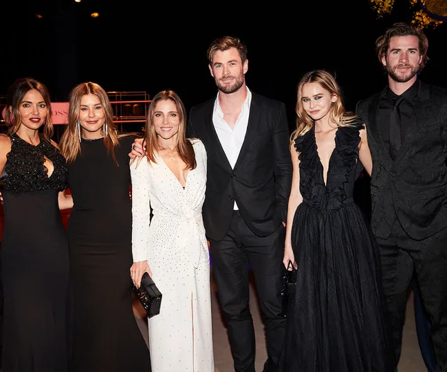 Group of six people dressed elegantly, standing together at an event, all smiling towards the camera.