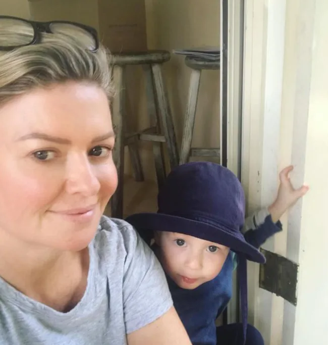 Woman with sunglasses and child in a dark hat indoors, smiling and looking at the camera.