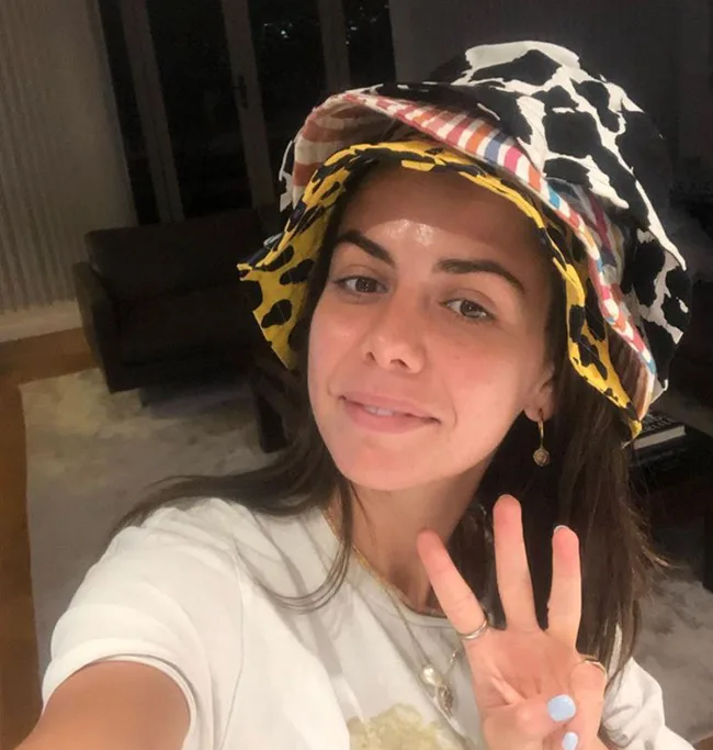 A person taking a selfie wearing a multicolored patterned hat and showing a peace sign indoors.
