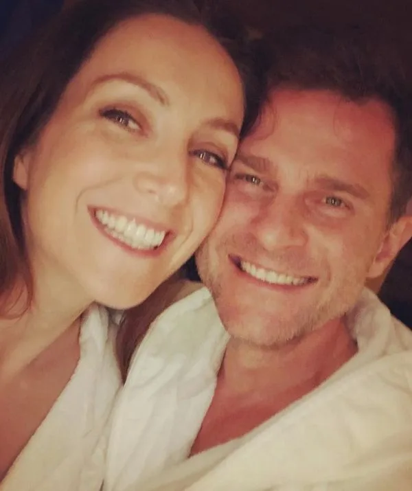 Man and woman smiling closely together, wearing white robes.