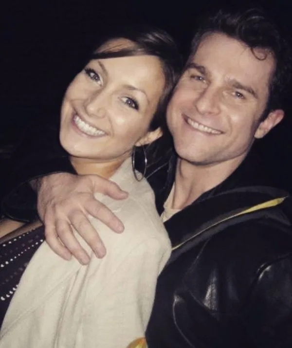 A smiling man and woman posing closely, with the man's arm around her shoulder.