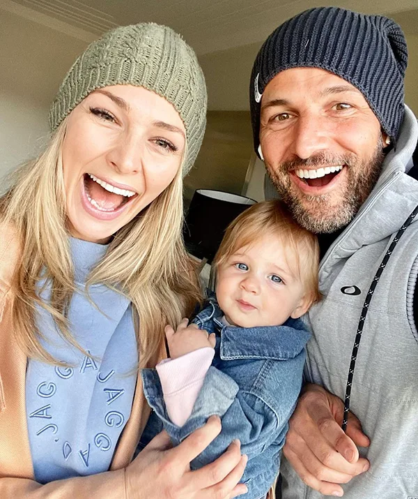 Family in beanies smiling with baby indoors.