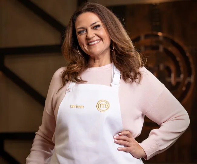 Image of a woman smiling in a light sweater and white apron with the name "Chrissie" embroidered on it.