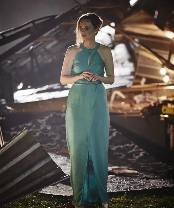 A woman in a teal gown stands amid debris in a dimly lit area.