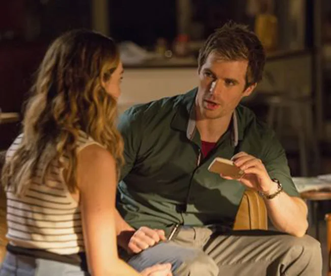 A man shows a card to a woman, sitting close together in a dimly lit room.