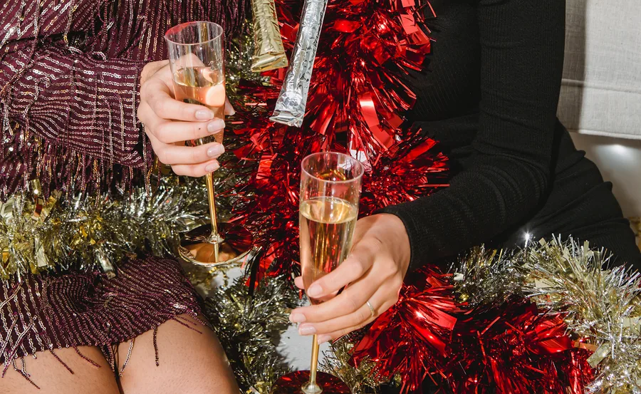 Two people holding glasses of champagne among festive red and gold tinsel decorations.