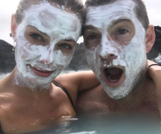 Two people with facial masks in a pool, one with an open mouth expression, both smiling.