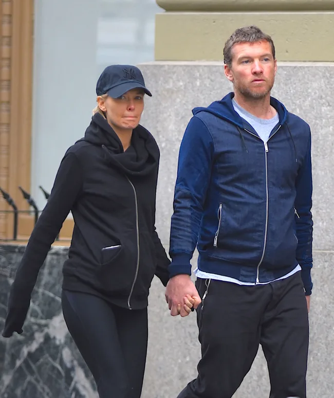 A couple walking hand-in-hand on the street, both wearing casual jackets and dark pants.