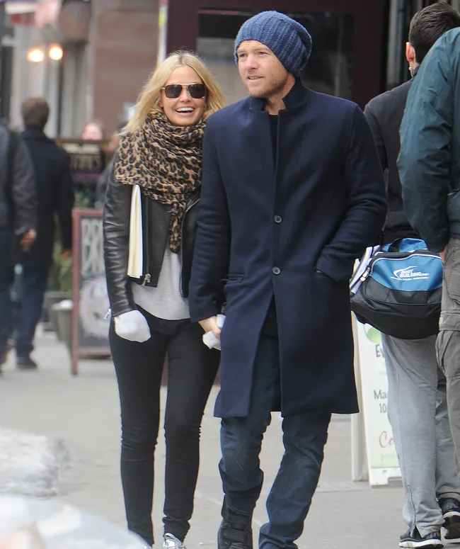 A man and woman walking on a city street, both casually dressed; woman wearing sunglasses and a leopard print scarf.