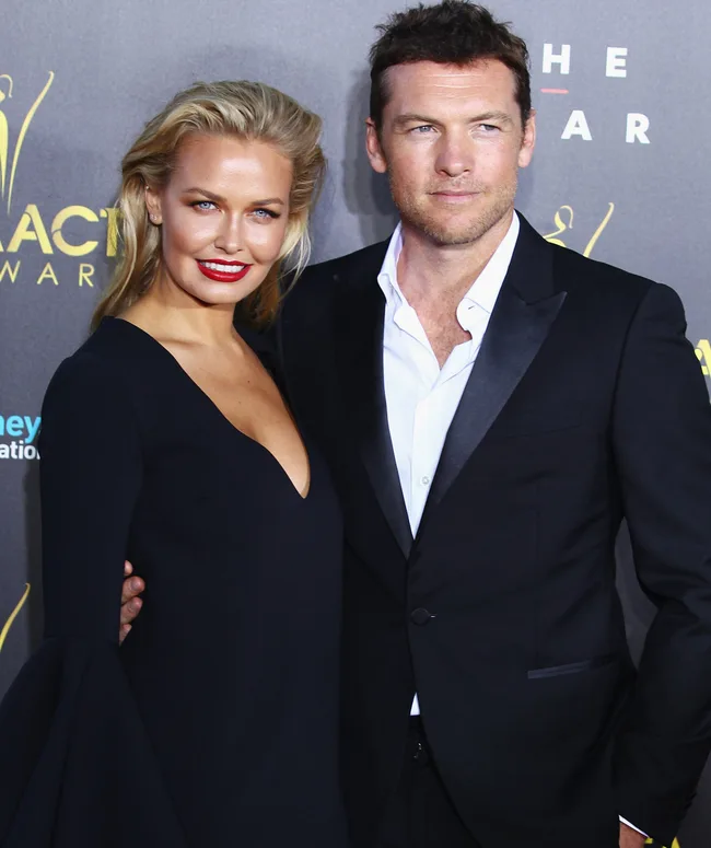 A couple poses on the red carpet at an event, both wearing formal black attire.