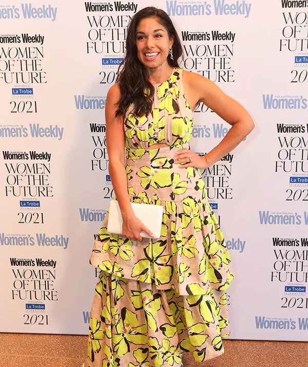 Woman in a floral dress at the "Women's Weekly Women of the Future 2021" event, smiling with clutch.