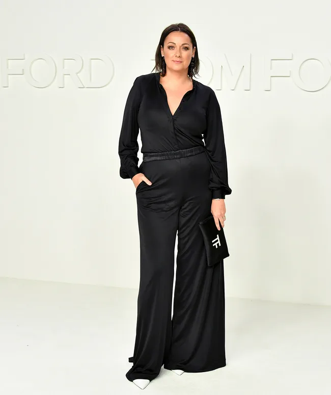 Person in a black outfit holding a black clutch with "TF" logo, standing against a light backdrop with "Tom Ford" text.