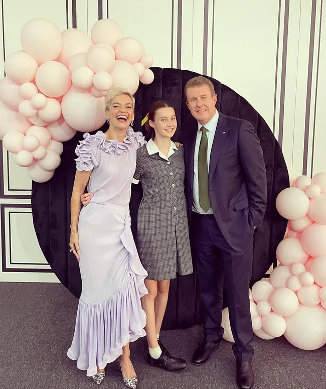 A smiling family poses in front of a black circular backdrop decorated with pink balloons.