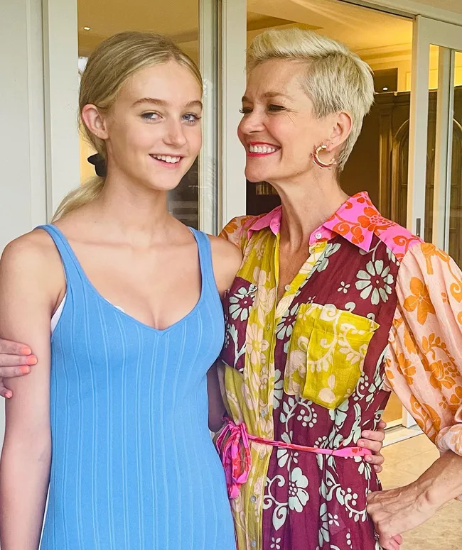 Two smiling women standing closely together, one in a blue dress and the other in a colorful floral dress.