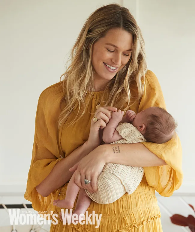 A woman in a yellow dress holds a baby lovingly, smiling down at the infant.