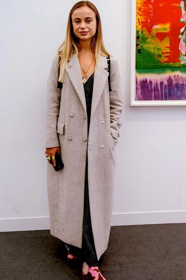 Woman in a plaid coat stands in a gallery with colorful abstract art on the wall.