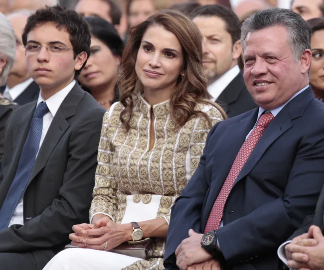 A group of people seated together, with a man in a suit on the right, a woman in an ornate dress, and a young man in a suit.
