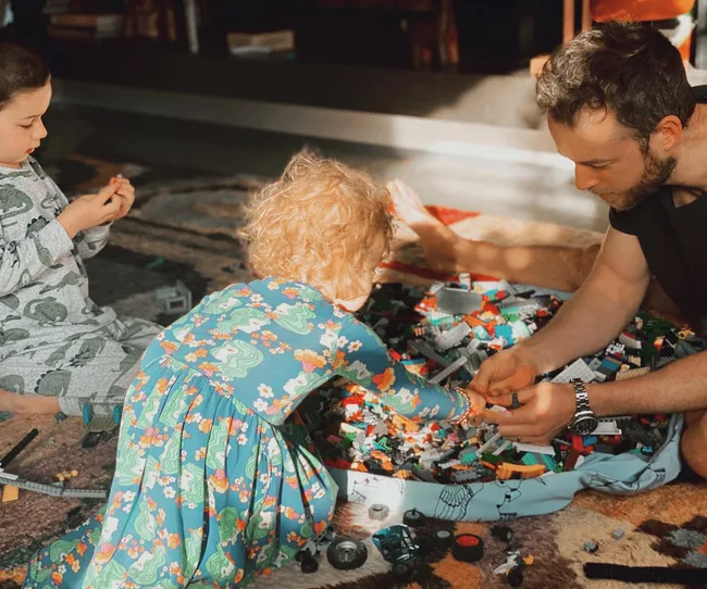 A man and two children building with LEGO bricks on a patterned rug.