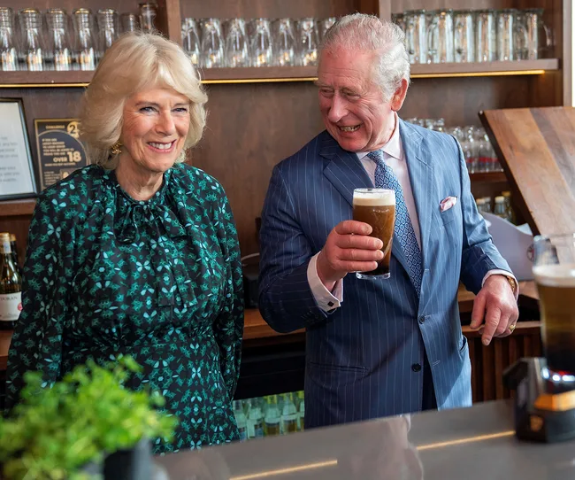 Two smiling people at a bar, one in a green dress and one in a blue suit holding a pint glass.