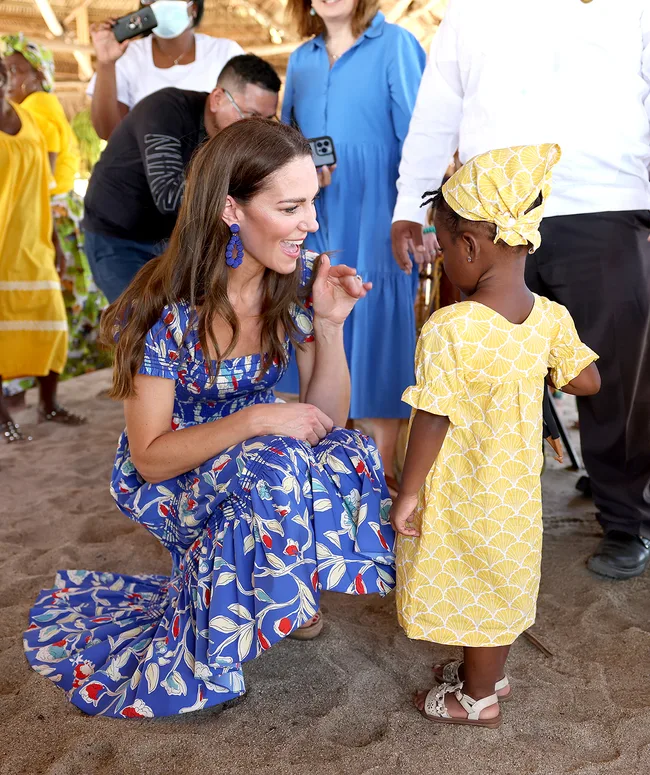 A woman in a blue floral dress interacts warmly with a child in a yellow dress at a vibrant outdoor gathering.
