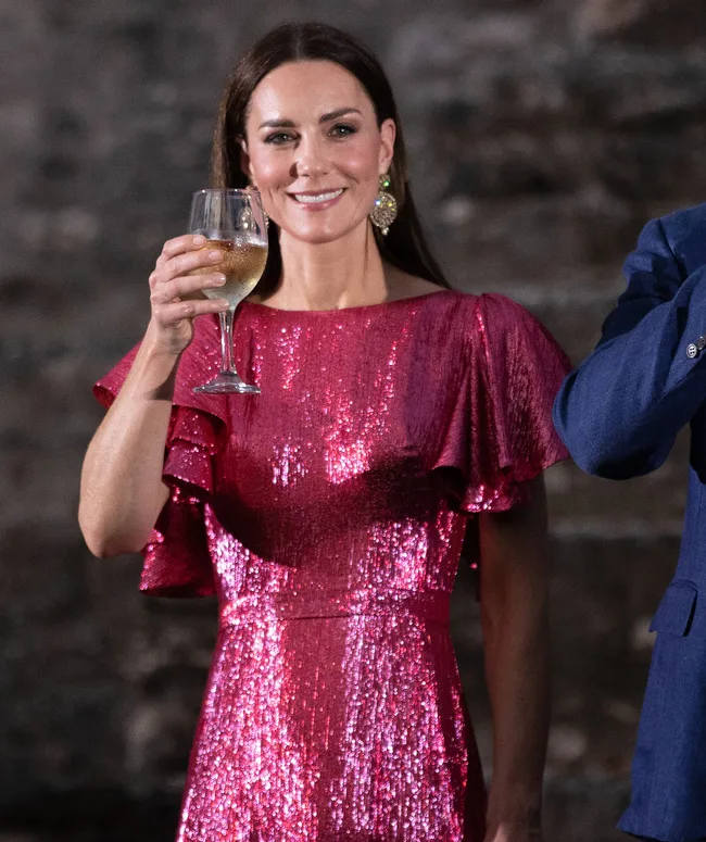 Woman in a sparkling pink dress holding a wine glass, smiling at an outdoor event.
