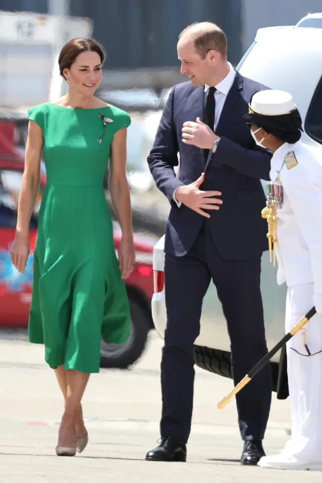 A woman in a green dress and a man in a suit greeted by a naval officer with medals.