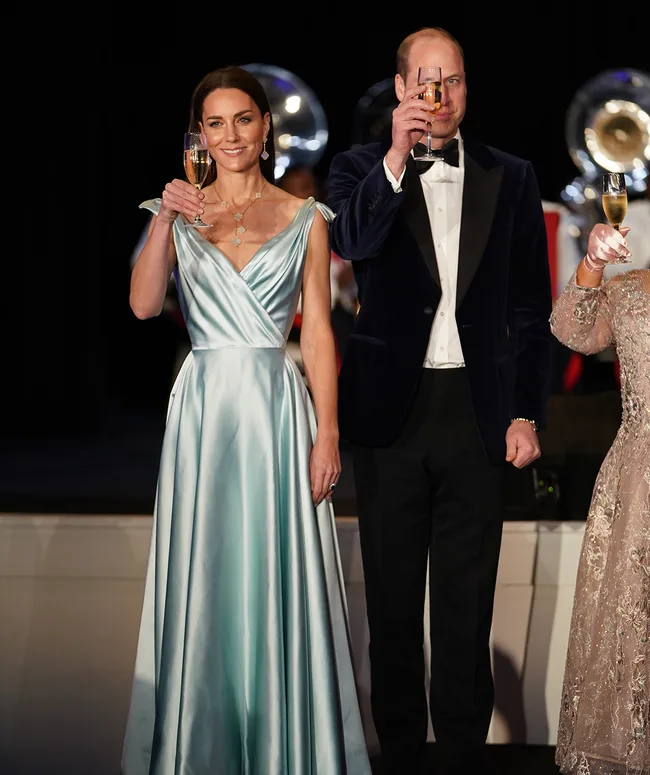A woman in a blue gown and man in a tuxedo raise champagne glasses at an elegant event.