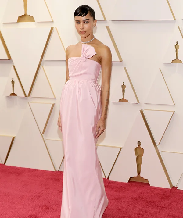 Woman in a pink gown on the red carpet at an awards event, standing in front of geometric wall decor.