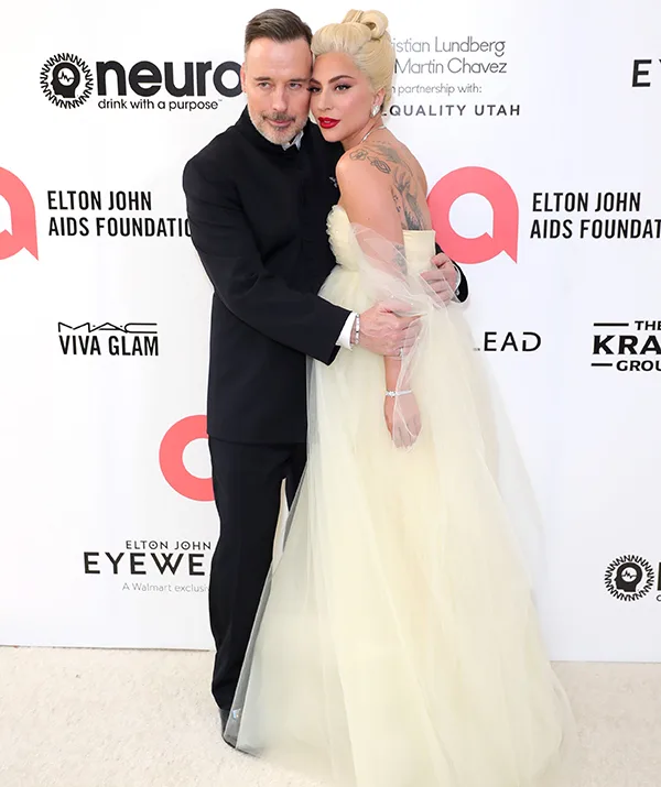 Man in black suit and woman in a yellow gown pose together at Elton John AIDS Foundation event.
