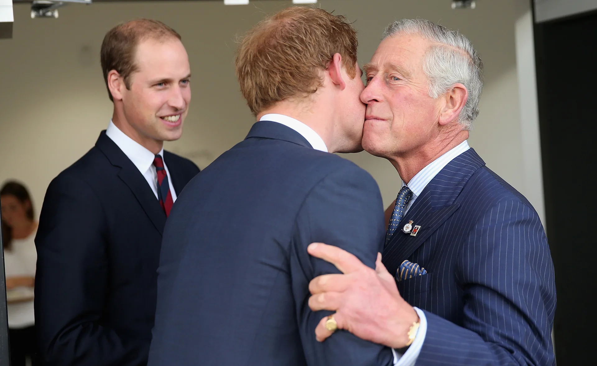 A man in a suit embraces another man, while a third man smiles in the background.