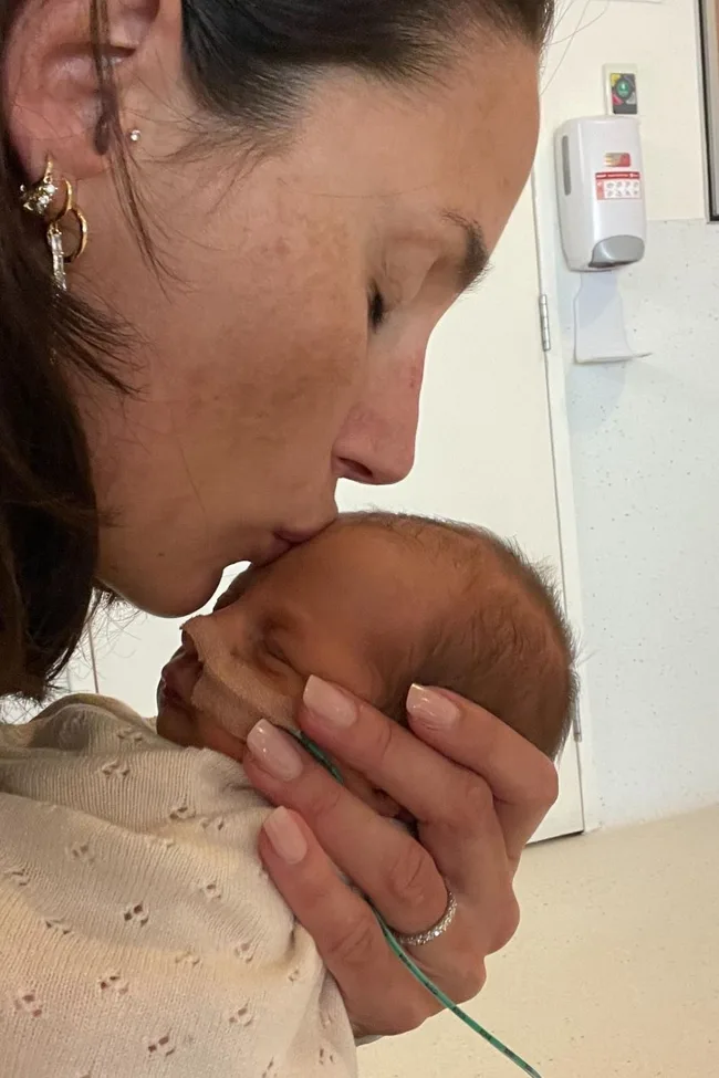 A woman gently kisses a newborn baby on the forehead in a tender embrace.