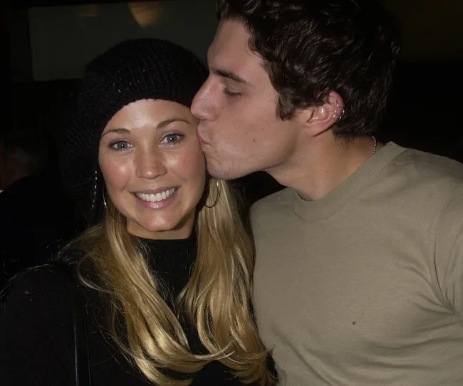 A man kisses a smiling woman on the cheek; she wears a black beret.
