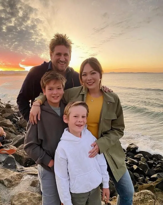 Family posing on a rocky beach at sunset with the ocean in the background.
