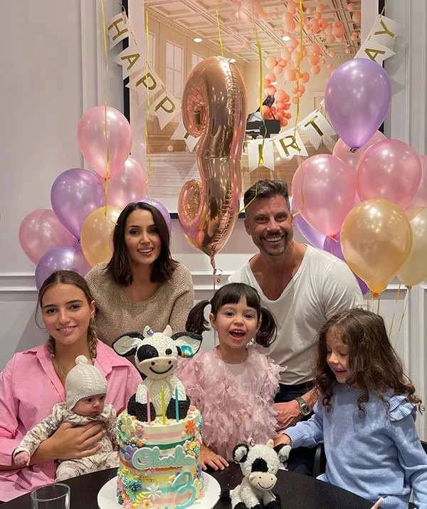 Family celebrating a child's third birthday with balloons, cake, and cow-themed decorations.