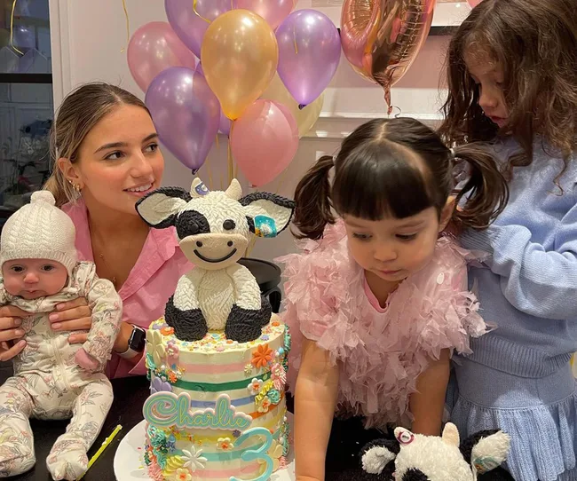 Children gathered at a birthday party with colorful balloons and a themed cake featuring a cow on top.