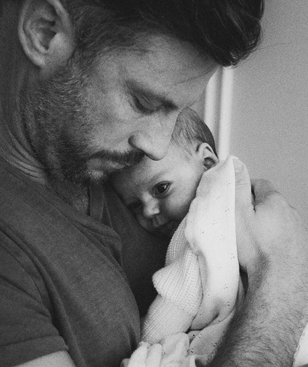 Father lovingly cradles a newborn baby, holding them close to his chest in a tender moment. Black and white photo.