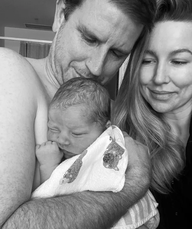 A couple lovingly holds their newborn baby wrapped in a patterned blanket, smiling and gazing at the child.